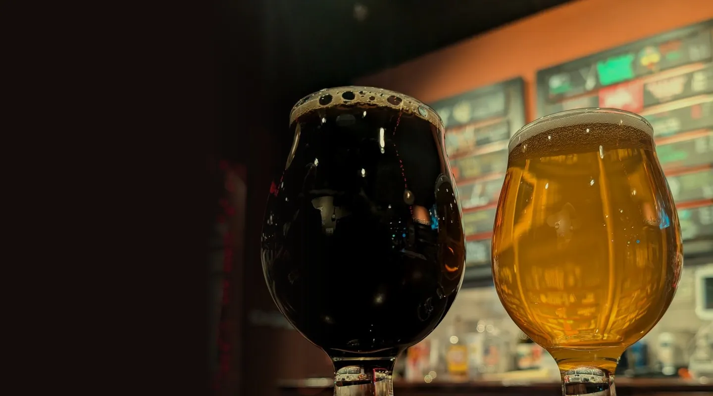 A stout and a pale ale on the bar in front of the painted tap boards